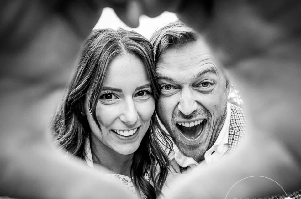 Couple de mariés souriant formant un cœur avec leurs mains, photographié en noir et blanc par un photographe de mariage à Troyes, dans un style reportage spontané et original.