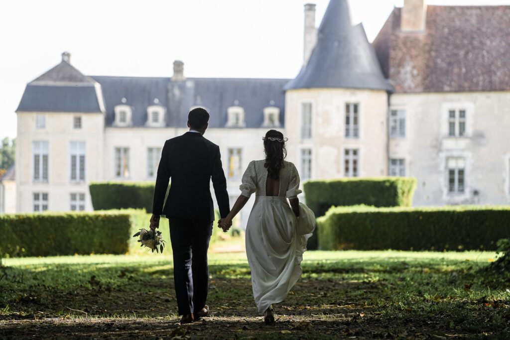 couple de mariés de dos marchant dans le parc arboré face au château de Riceys-Bas