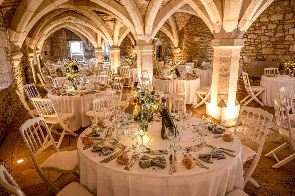 Cave voûtée du château de Riceys-Bas décorée pour un dîner de mariage, tables rondes élégantes, lumière chaleureuse et ambiance intimiste en Champagne.