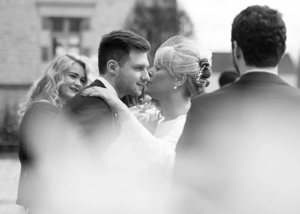 La mariée embrasse un proche lors des félicitations, capturé en noir et blanc pendant un mariage.