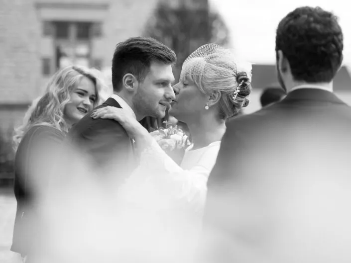 La mariée embrasse un proche lors des félicitations, capturé en noir et blanc pendant un mariage.