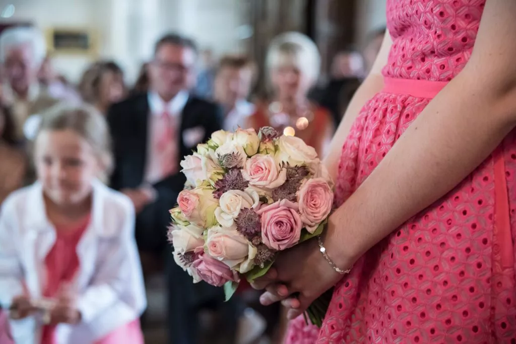 Bouquet de fleurs tenu par une demoiselle d’honneur pendant la cérémonie, les invités flous en arrière-plan, instant capté sur le vif.