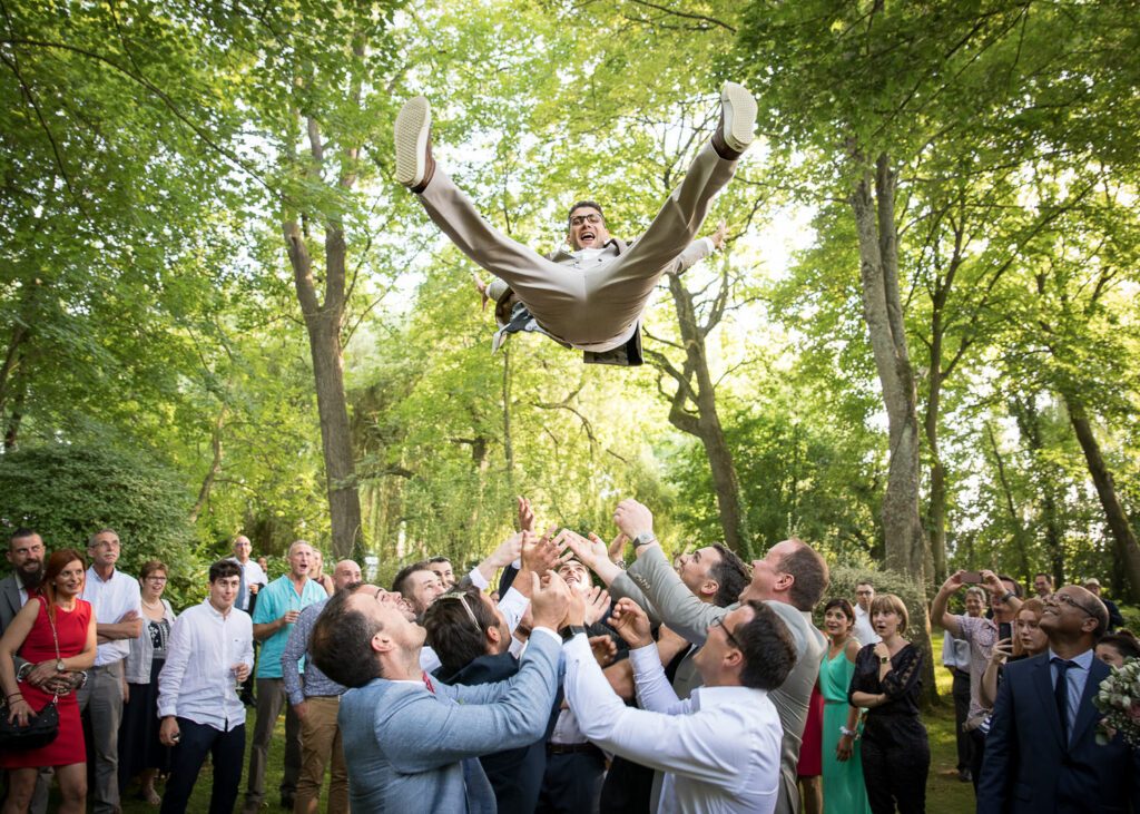 Le marié est lancé en l’air par ses amis lors d’un mariage en extérieur.