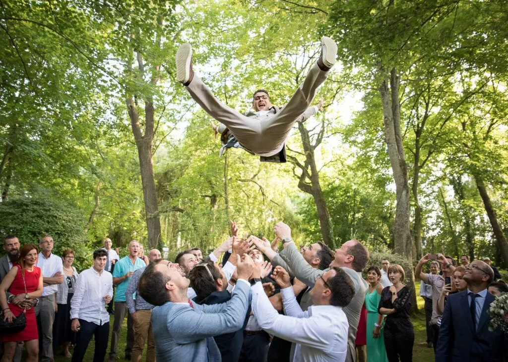 Le marié est lancé en l’air par ses amis lors d’un mariage en extérieur.