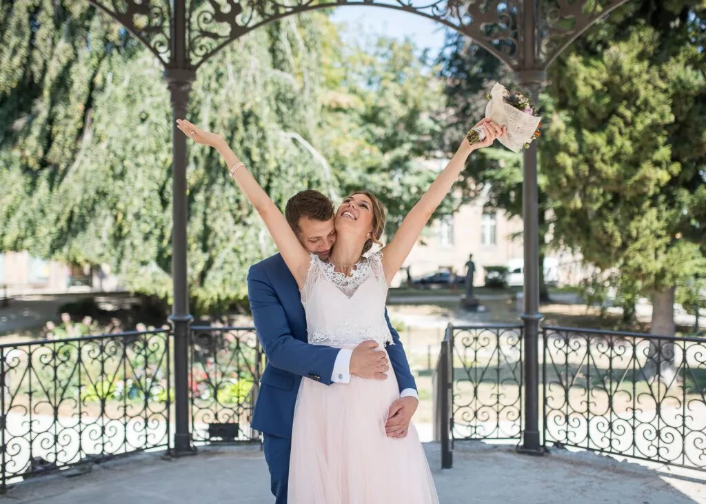 Moment de tendresse des mariés enlacés sous un kiosque lors d’un mariage.