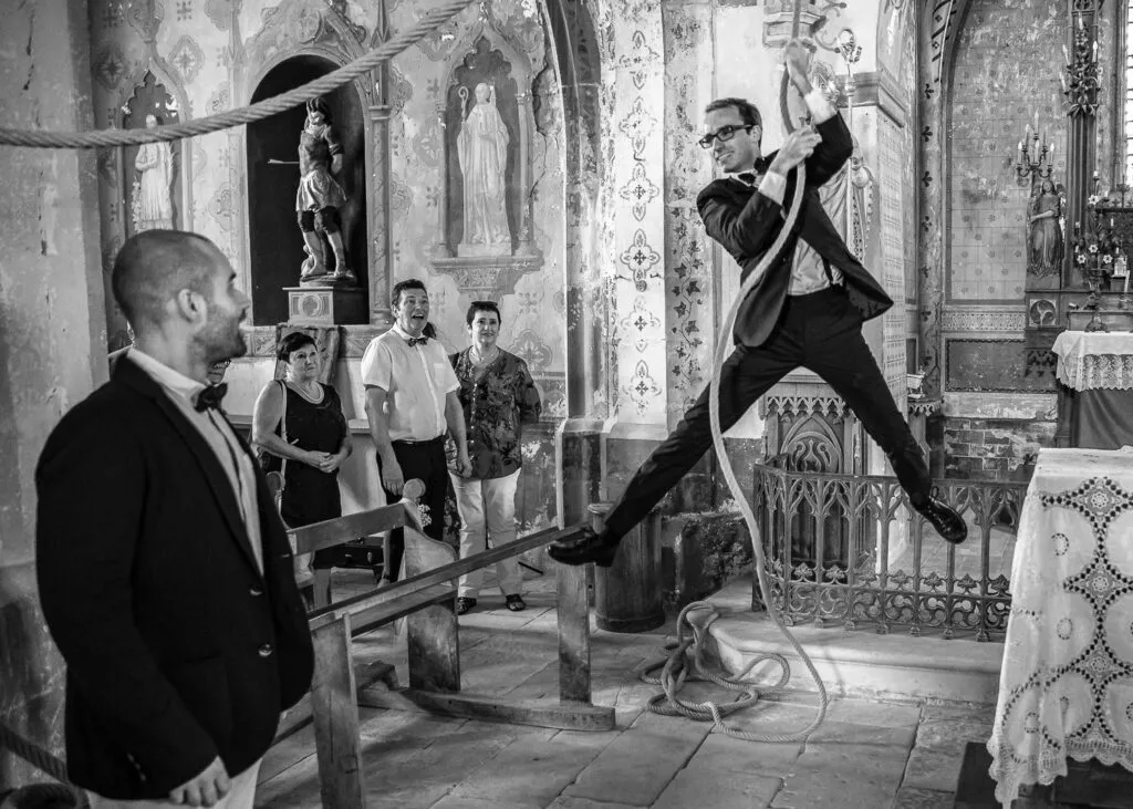 Un garçon d’honneur se balance à une corde à l’intérieur de l’église pendant un mariage, en noir et blanc.