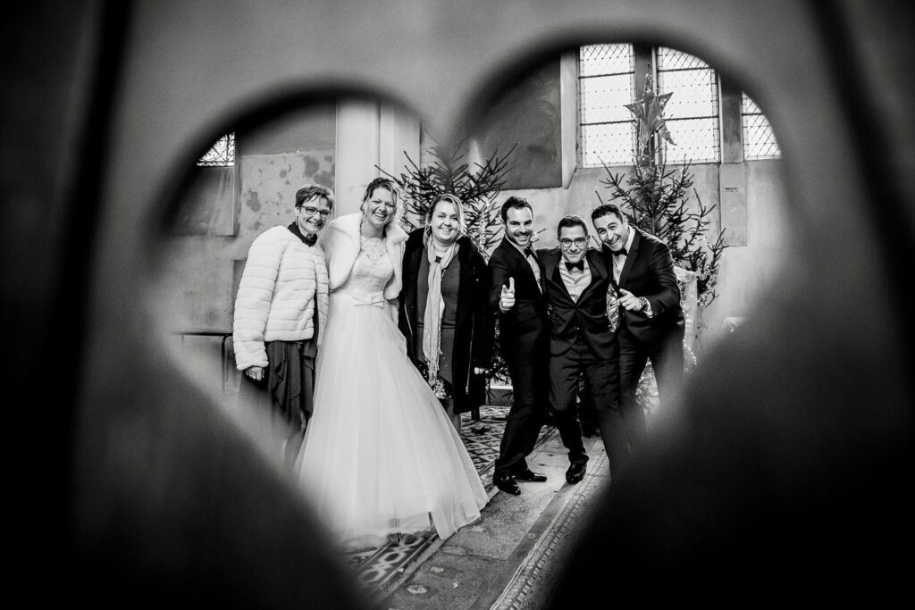 La mariée entourée de ses proches, photographiée à travers un cœur lors d’un mariage, en noir et blanc.
