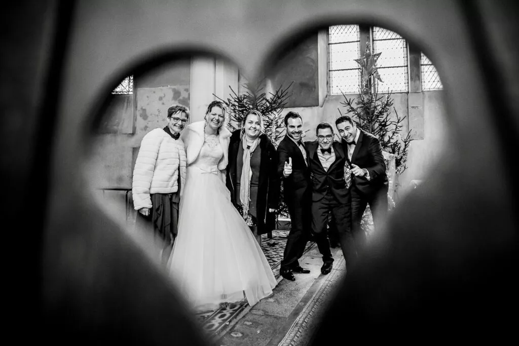 La mariée entourée de ses proches, photographiée à travers un cœur lors d’un mariage, en noir et blanc.