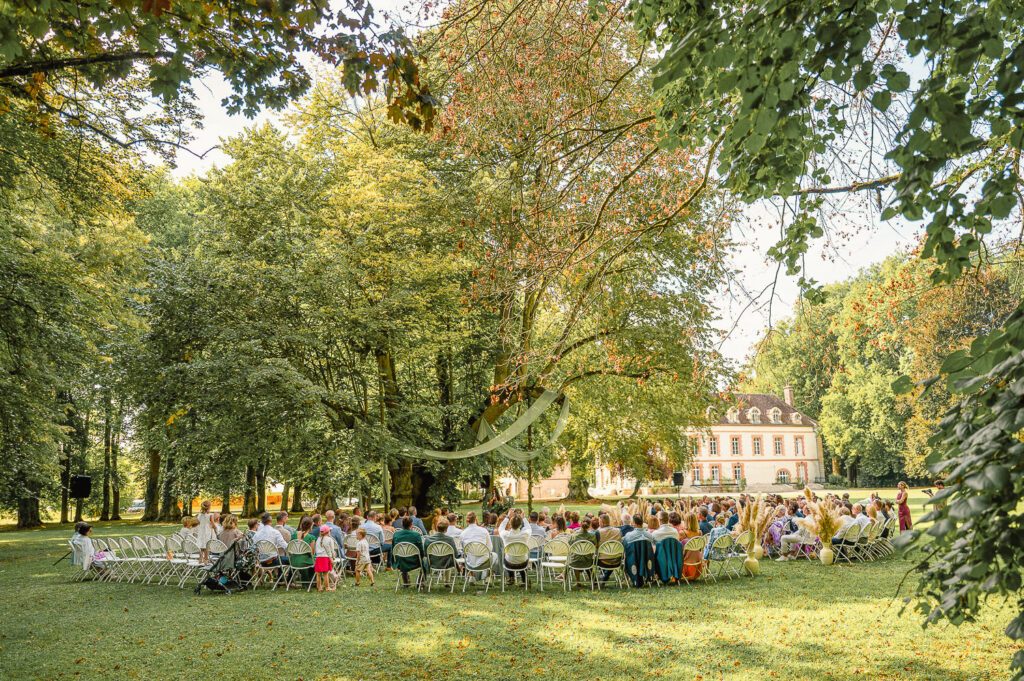 Cérémonie de mariage en plein air, les invités réunis dans le parc d’un domaine.