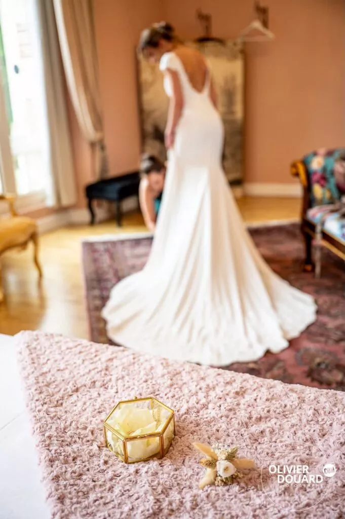 Mariée pendant les préparatifs au chateau de Percey avec sa témoin qui ajuste la robe et les alliances au premier plan
