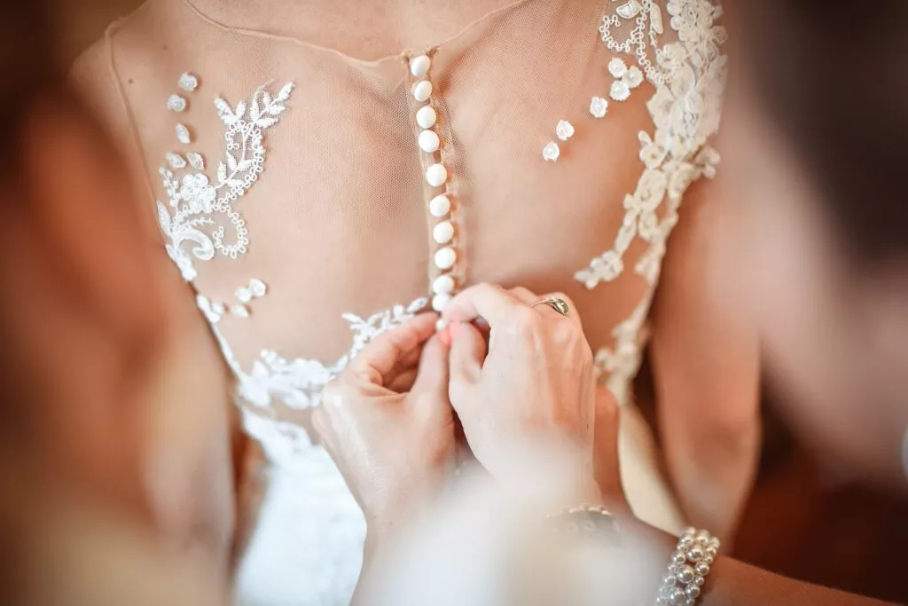 Gros plan sur le boutonnage de la robe de mariée en dentelle lors des préparatifs au Domaine de Vauluisant près de Troyes, détail élégant d’un reportage photo de mariage.