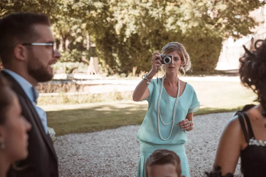Invitée photographiant la scène avec un appareil compact pendant le vin d’honneur au Domaine de Vauluisant près de Troyes, moment spontané d’un mariage en extérieur.