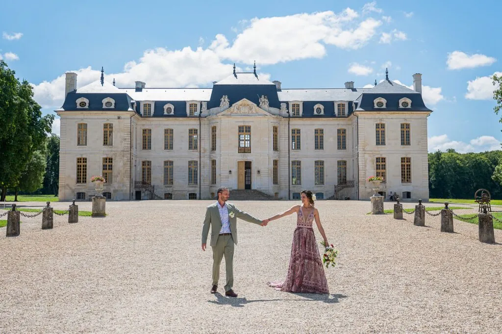 Les mariés tout sourire en se tenant la main devant le château de Vaux