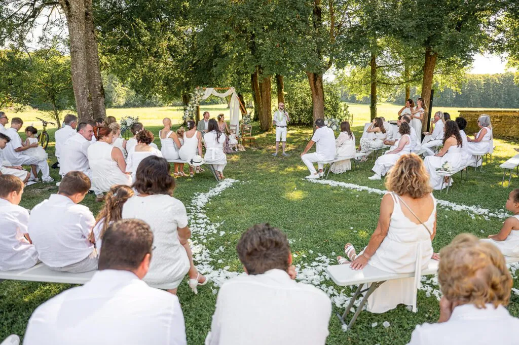 les invités du mariage sont habillés en blanc pendant la cérémonie laïque sous les arbres