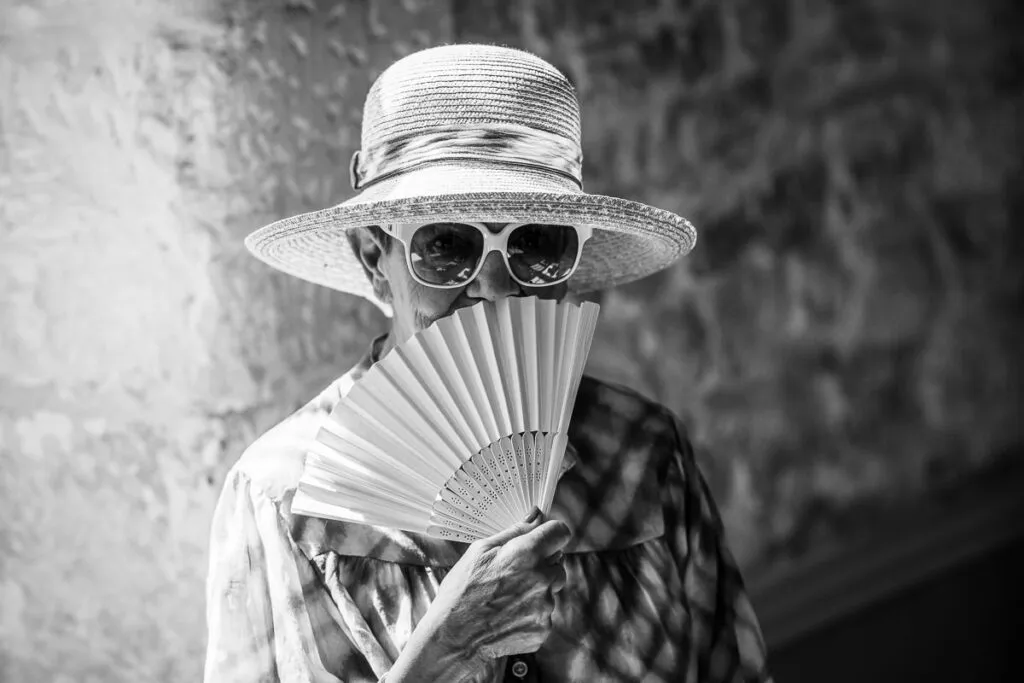 Une dame avec son chapeau, lunettes de soleil et son éventail donne une photo très graphique et le noir et blanc fait ressortir ce joli moment