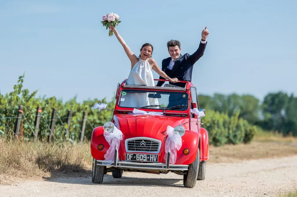 Les mariés saluent depuis l'ouverture du toit de la citroen 2ch rouge
